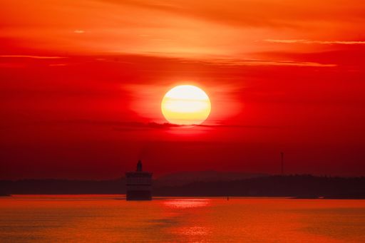 A stunning sunset over the ocean with a lighthouse silhouette and vibrant red and orange sky