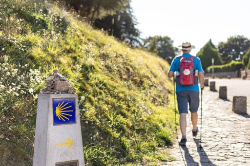 Pilgrim walking to Santiago de Compostela in Camino de Santiago pathway guided by milestone sign with scallop shell and arrow indicating the way