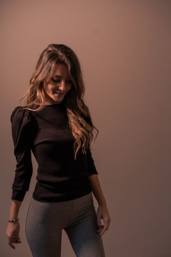 A vertical shot of a young Caucasian woman standing in front of a brown wall and posing while smiling