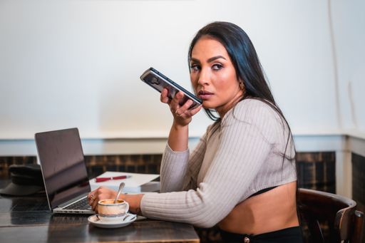 A closeup of a young Hispanic woman sending an audio message on her phone while having a coffee