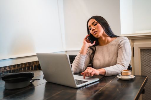A young woman sitting in a coffee shop with a laptop and talking on the phone