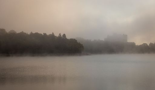 A serene misty morning landscape over a calm lake with soft sunlight breaking through the fog