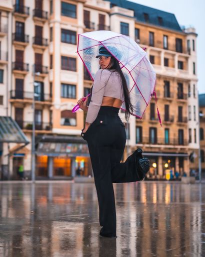 A vertical shot of a beautiful Latina posing on a rainy day in Spain while holding a clear umbrella