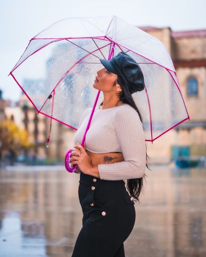 A woman standing under the rain in the street with an umbrella and looking up