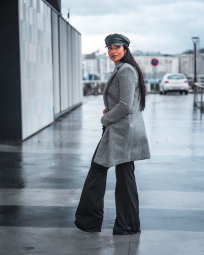 A vertical shot of a classy Spanish woman posing outside on a rainy day, wearing an overcoat and a cap