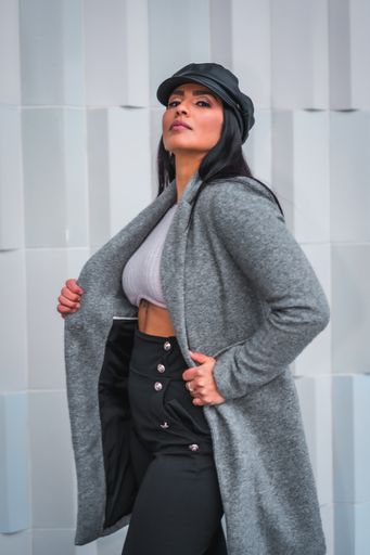 A vertical shot of a stylish young Latina posing in a winter coat in front of a gray wall