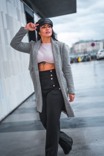 A vertical shot of a stylish Latina posing outside on a rainy day touching her leather hat