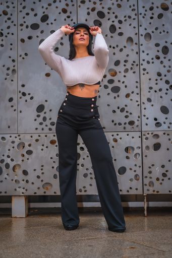 A vertical shot of a fierce Latina striking a pose in front of an abstract gray wall