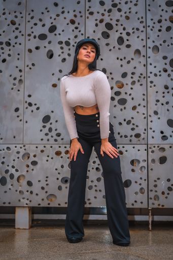 A vertical shot of a young brunette Latina with a black hat on posing in front of an abstract wall