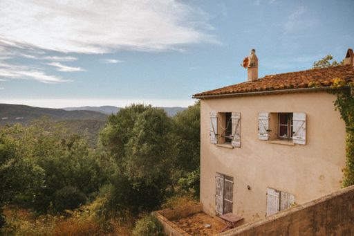 An old house with white windows and tiled roof in Gassin village in the French Provence with background of trees and sky