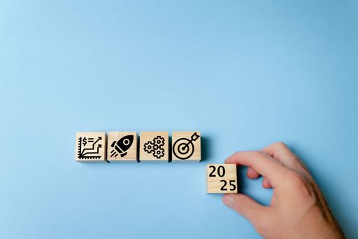 A hand is placing a wooden block with "2025" on it next to other blocks with symbols for growth, innovation, teamwork, and goals.