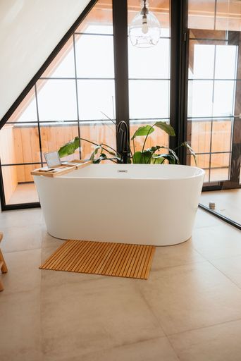 Modern bathroom with a freestanding tub, wooden mat, and large windows offering natural light.
