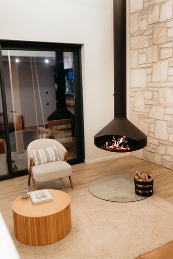 A cozy modern living room with a hanging fireplace, armchair, coffee table, and stone wall.