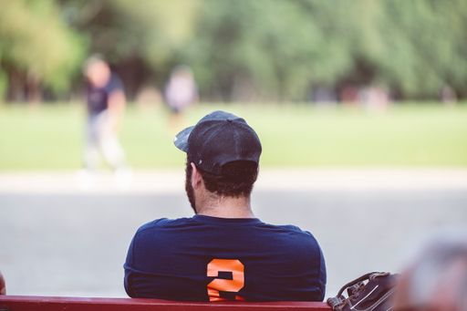 A back view of a young male wearing a t-shirt and cap sitting in a park