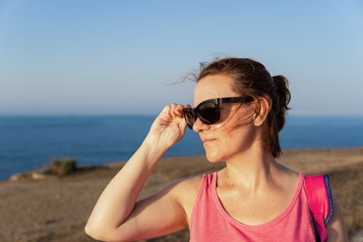 Close up view of a Portrait of a Beautiful Caucasian woman putting on her sunglasses at sunset in a park near the sea.