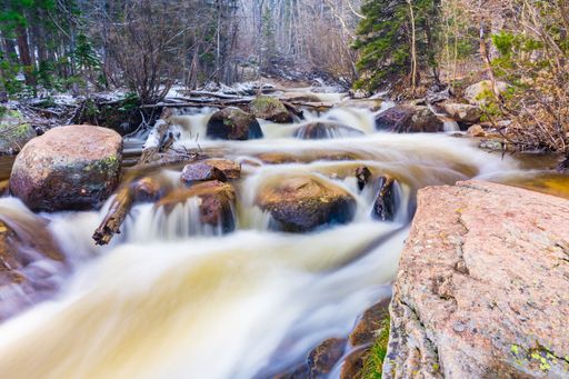Long exposure shot of a flowing river with rocks and trees in a forest setting.