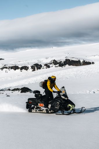 A person enjoying ride on a snow sledge down a snowy hill in a deep winter landscape on a sunny day with clear sky and white clouds