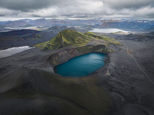 A stunning aerial view of a volcanic crater lake surrounded by rugged terrain and mountains under a cloudy sky in Iceland.
