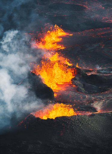 Aerial view of an active volcanic eruption with bright orange lava and dark smoke in Iceland.