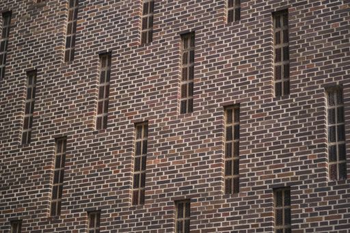 A low angle shot of a building brick wall with detail with high and narrow windows