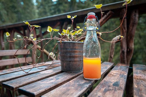 A half-filled bottle of juice on a wooden table with a potted plant