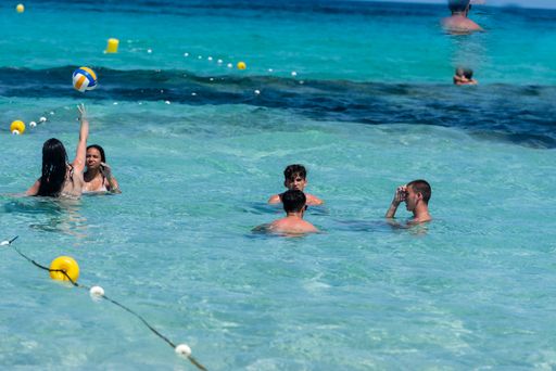 A close up of people in the sea in Formentera, Spain with rocky hill in background on a summer day