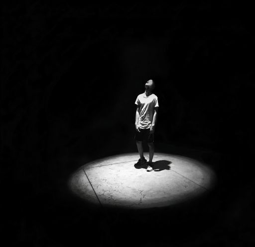 A grayscale shot of a young man in casual clothes place under a spotlight against a black background