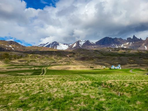 A scenic Icelandic landscape featuring a blue house and snow-capped mountains under a clear sky.