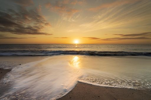 A serene beach sunset with golden hues and gentle waves washing ashore, creating a peaceful and calming atmosphere.