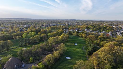 Aerial view of a lush green golf course surrounded by residential areas and trees on a clear day.