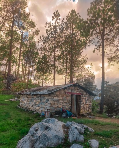 A stone cabin surrounded by trees in the woods on a cloudy day
