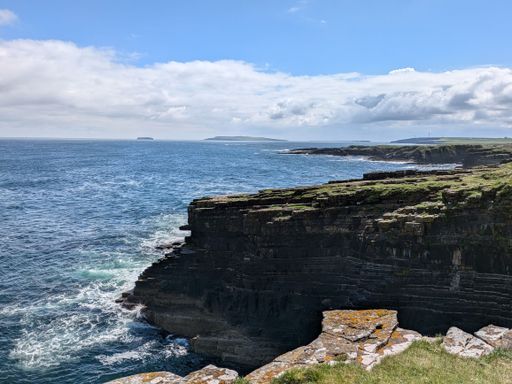 A scenic view of coastal cliffs and the ocean under a partly cloudy sky in Orkney, Scotland