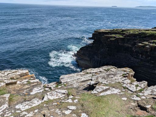 A scenic view of a rocky coastline with waves crashing against the cliffs under a clear sky.