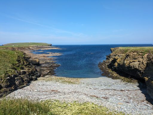 A scenic coastal landscape with cliffs, rocky shoreline, and clear blue ocean under a bright sky.