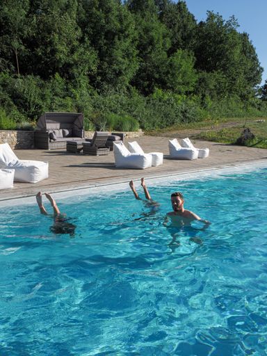 A vertical shot of a Caucasian man in the pool with two upside-down women, on a sunny day