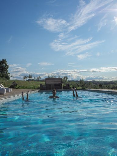 A vertical shot of a Caucasian man in the pool with two upside-down women, on a sunny day
