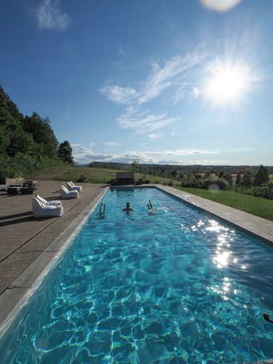 A vertical shot of a Caucasian man in the pool with two upside-down women, on a sunny day