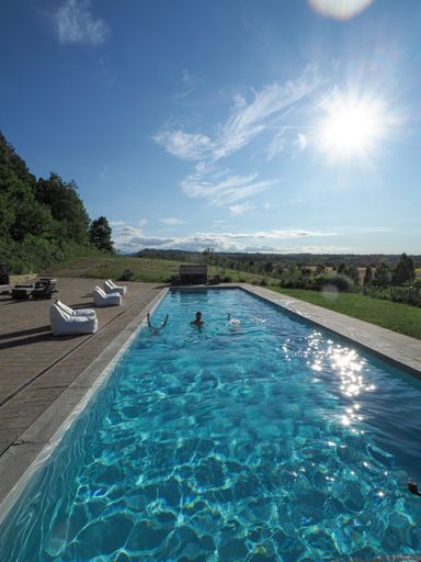 A vertical shot of a Caucasian man in the pool with two upside-down women, on a sunny day