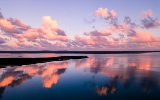 A beautiful sunset over a calm lake with pink clouds reflecting on the water.
