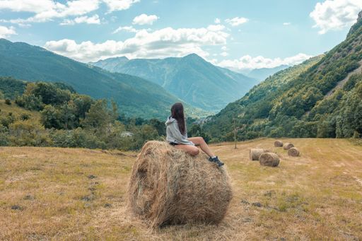 A young girl sitting on a round hay bale on top of a hill