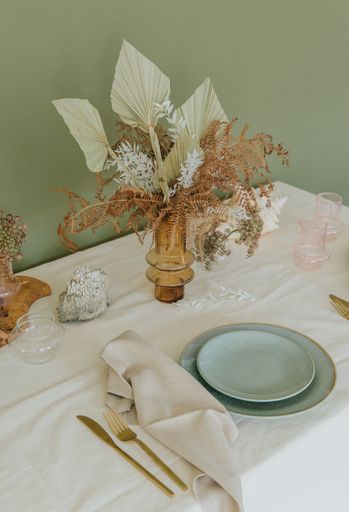 A beautifully decorated table with a vase flowers and tableware on the green background