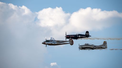 A view of three vintage military aircrafts performing an airshow maneuver against a backdrop of blue sky and clouds.