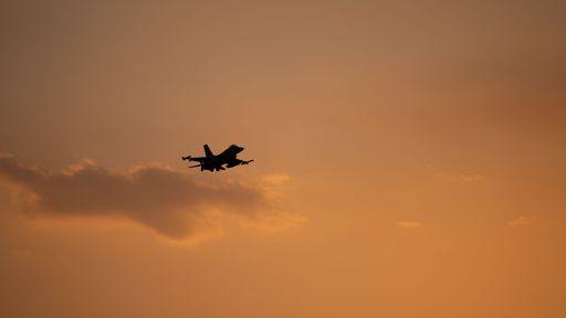 Silhouette of a fighter jet flying against an orange sunset sky