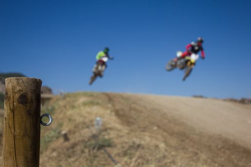 The two motocross racers in action jumping over the hill against a clear blue sky