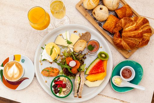 A top view of croissants, different pastries with a cup of latte and orange juice with other tasty snacks beautifully arranged on a table