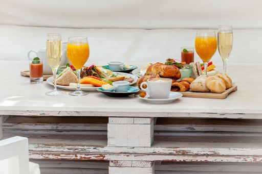 Croissants, different pastries with a cup of latte, orange juice, tea, champagne, and other tasty snacks beautifully arranged on a table