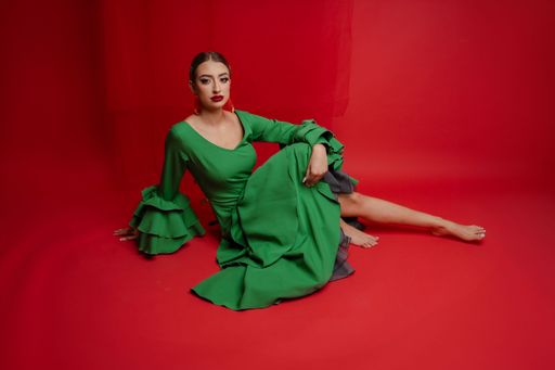 A woman in a green dress poses against a red background, showcasing fashion and contrast.