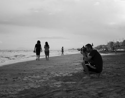A grayscale shot of a photographer taking a photo on a sandy beach