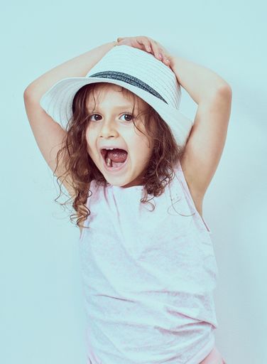 A happy young Hispanic blonde girl wearing hat against a light blue background