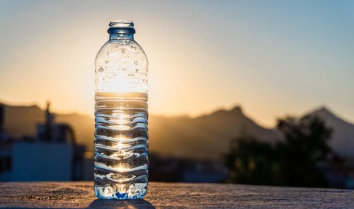 A shallow focus of a plastic water bottle standing with shiny sunlight with blurred park in background
